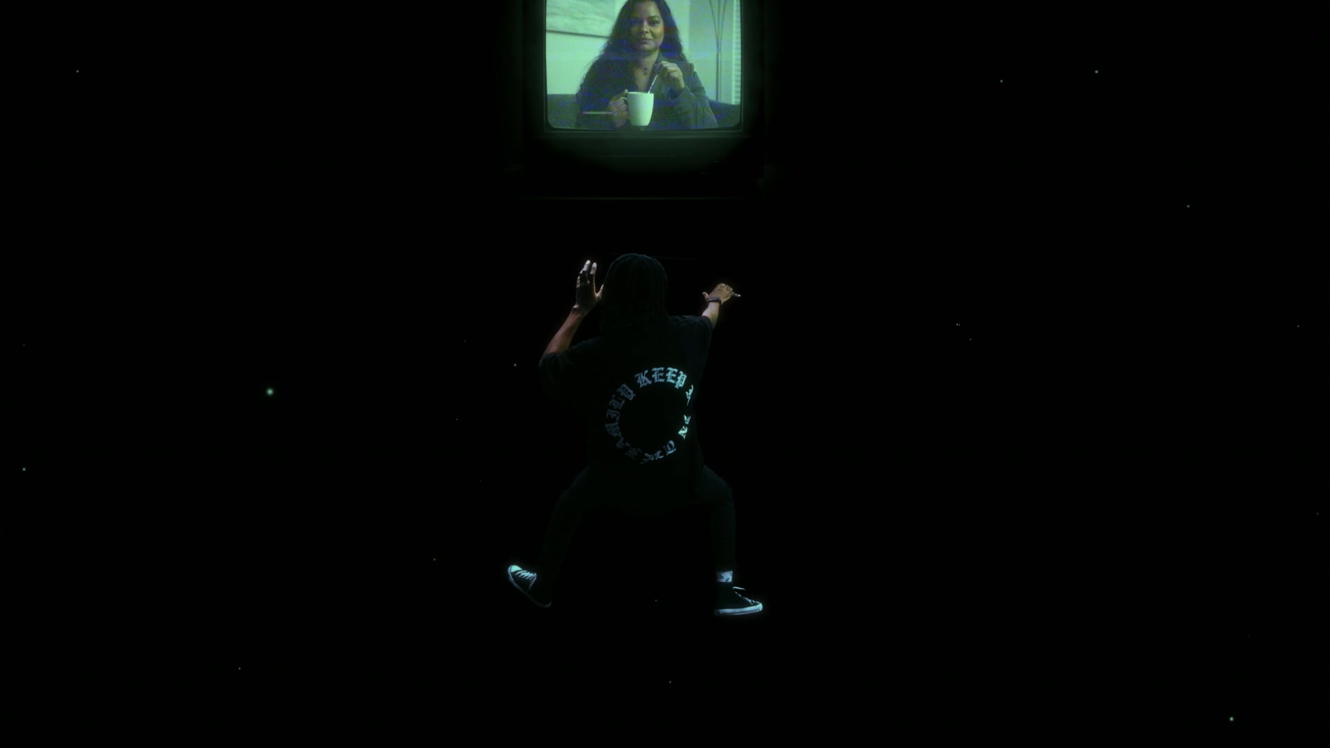 The rear-facing figure reaches toward the screen. The screen acts as a visual anchor, giving the black environment a direction and a sense of distance.